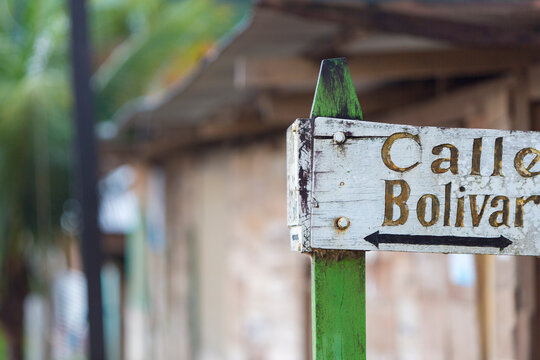 Old wooden sign pointing the direction to the Street Bolivar in Rurrenabaque with blurred background.
