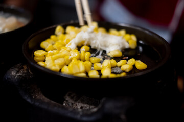 Hand hold chopsticks with cheese mix on seed corn in hot pan