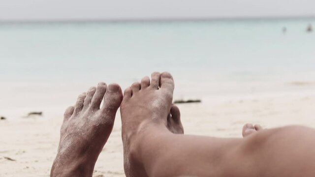 POV of Feet of a young couple of men and women lying on a tropical sandy beach near Ocean. Male and female legs sunbathe and relax on the exotic resort. Romantic vacation for couple in love. Zanzibar