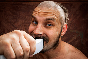 Caucasian man trying to shave with an electric razor. A brutal bald man holds a razor in his hand...