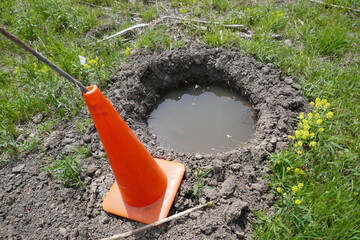 Flooded water filled hole with traffic cone marking danger