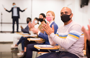 Portrait of male participant of business event in face mask applauding speaker at conference