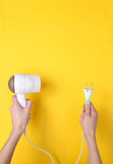 Hand holding White hair dryer and plug on yellow background. Beauty concept. Hair care, hair style. Top view. Flat lay.