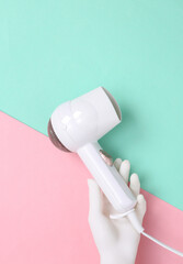 Fototapeta premium Hand holding White hair dryer on pink blue background. Beauty concept. Hair care, hair style. Top view. Flat lay. Copy space