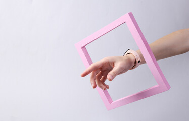 Female hand through a pink frame on a gray background. Minimalism