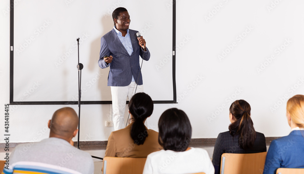 Wall mural successful aframerican business coach speaking from stage to audience at corporate training