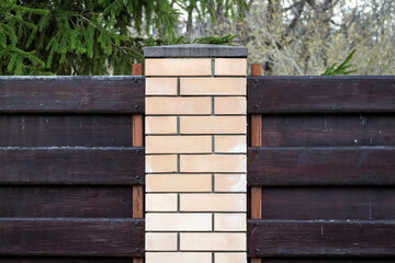 A fence around the territory of a private house made of bricks and boards.