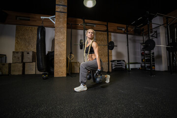 Fit woman in sportswear doing lunges with a kettlebells in hands in gym. Functional training