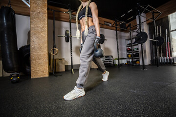 Fit woman in sportswear doing lunges with a kettlebells in hands in gym. Functional training