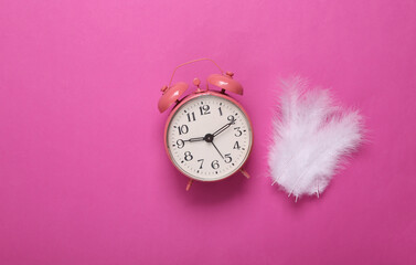 Soft feathers and alarm clock on pink background. Minimalism. Top view. Flat lay