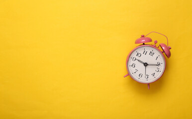Pink alarm clock on yellow background. Copy space. Top view. Flat lay