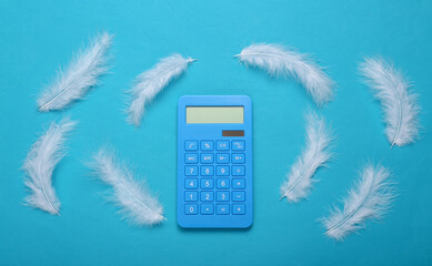 Soft feathers and calculator on blue background. Minimalism. Creative layout. Top view. Flat lay