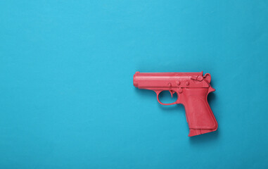 Pink pistol gun on blue background. Creative concept. Minimalism Flat lay. Minimal layout.Top view