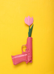 Origami flower from the barrel of a pink gun on yellow background. Creative romantic concept....