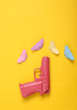 Pink pistol gun with with origami butterflies on yellow background. Creative concept. Minimalism Flat lay. Minimal layout.Top view