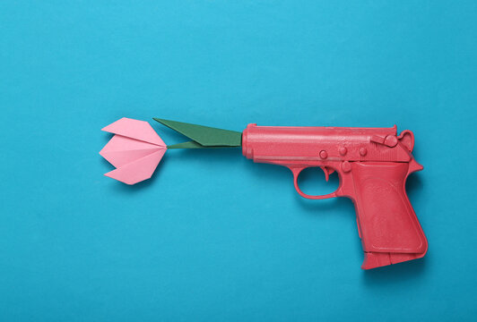 Origami flower from the barrel of a pink gun on a blue background. Creative romantic concept. Minimalism love Flat lay. Minimal layout.Top view