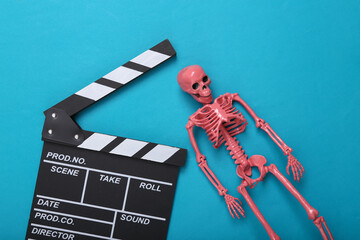 Halloween horror movie. Movie clapperboard and pink skeleton on a blue background. Top view. Flat lay
