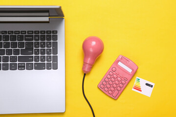 Laptop, Pink light bulb with graph class of energy consumption and calculator on yellow background....