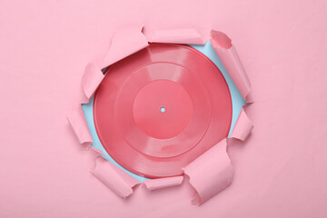 Creative music layout. Pink vinyl record through torn hole of pink blue paper. Pastel color trend....