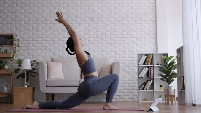 Asian woman look laptop practice yoga warrior pose online course at home