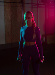 Fototapeta na wymiar Young fit slim woman with dumbbells in her hands in pink green neon gradient light at gym. Sport, fitness, lifestyle concept