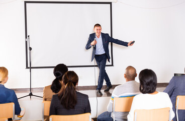 Naklejka na ściany i meble Emotional business coach speaking from stage to audience, giving corporate motivational training