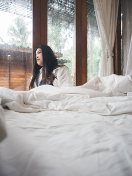 Depressed Young Woman Near Window In Bedroom At Home With Rainy Atmosphere.