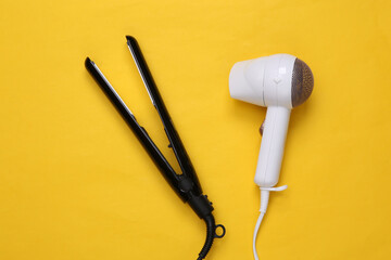 White hair dryer and hair straightener on yellow background. Beauty concept. Top view. Flat lay
