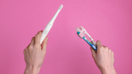 Female hand holds a modern electro-toothbrush with charger on pink background. Top view