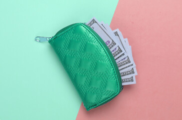 Green wallet with hundred dollar bills on green-pink pastel background. Top view
