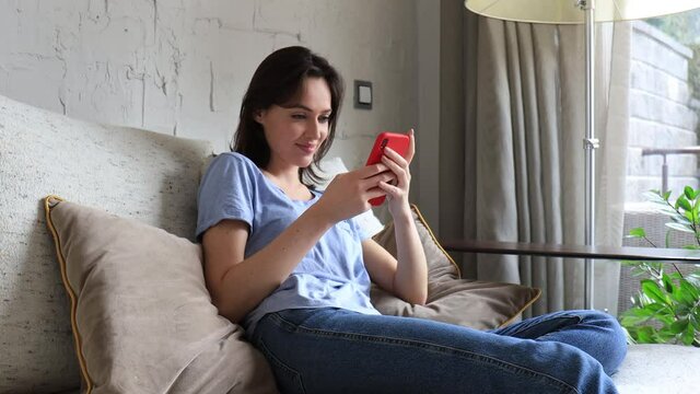 Attractive young woman sitting of the sofa at home using phone and smiling. Feeling happy. Communication female looking message at cell phone or smartphone.