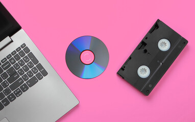 Flat lay composition of laptop, cd disc, audio cassette on pink background. Retro storage media. Top view