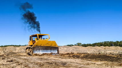 A big yellow d8K bull dozer blowing a big black thick ploom of dirty smoke into the air as it's about to do another push.