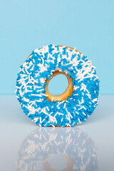 Donut with blue and white sprinkles on blue background with copy space.