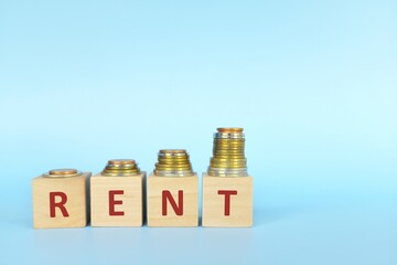 Rent increase concept. Word rent on wooden blocks in blue background with increasing stack of coins.