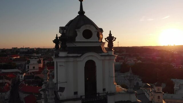 Aerial. Beautiful sunset, drone fly around the bell tower of St. John's church in Vilnius, Lithuania, Europe. (sventu jonu varpine). Sun rays shines through the roof. Old town in the background.