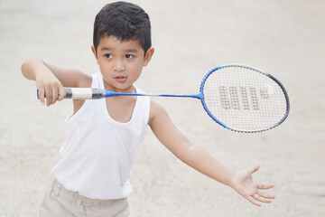 Asian boy 3 year old holds a badminton racket and he makes a very happy laughing face Outdoor exercise concept.