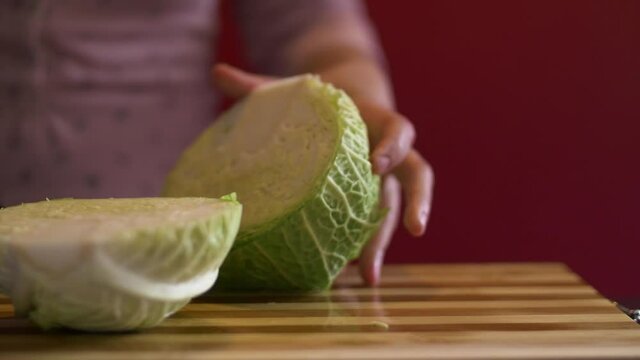 Close-up shot of woman's hands slicing a savoy cabbage in half before cooking