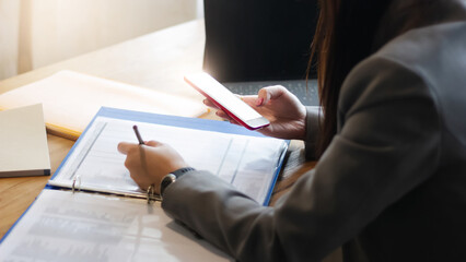 Focus on hand, asian businesswoman in suit holding smart phone and The other hand blurred while write on paperwork