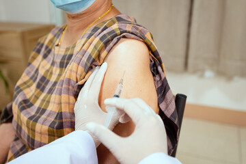 Close up on doctor is injecting vaccination on senior woman arm. Adult patient wearing protective...