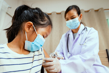 Doctor injecting vaccination on asian child girl arm. Doctor and child patient wearing protective...