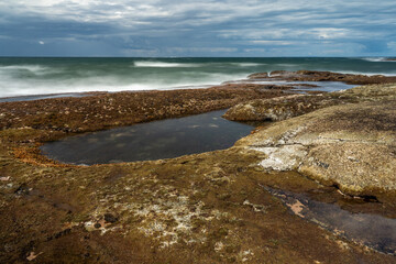Green sea with a blue cloudy sky and rock pool