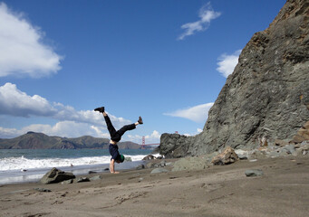 Man does a Handstand in on beach in front of the Golden Gate Bridge