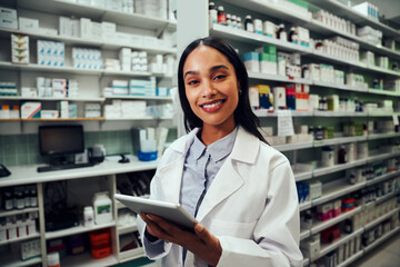 Happy woman working in pharmacy using digital tablet wearing labcoat looking at camera