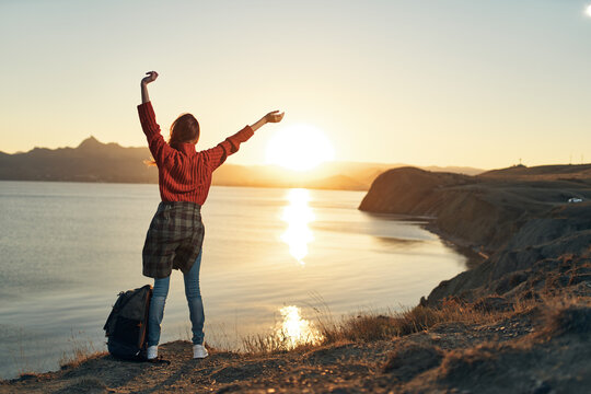 woman tourist with hands raised up horizon sunset back view