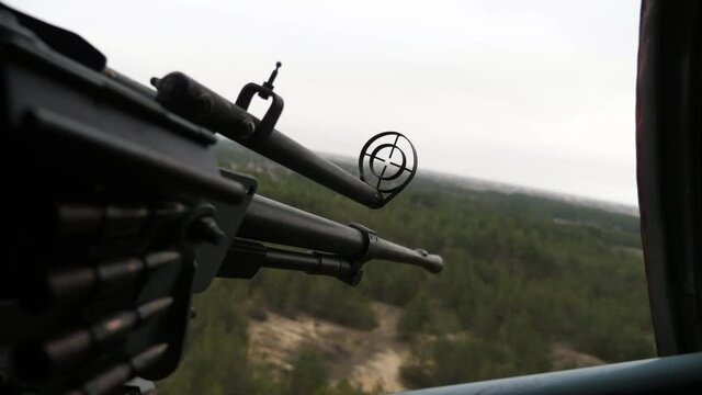 Warring machine gun with a cartridge tape is aimed at forest objects from a chopper