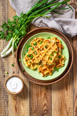 Not sweet waffles with potatoes, peas, bell peppers, cheese are served with sour cream and herbs on a plate on a rustic table. Top view flat lay. Copy space.