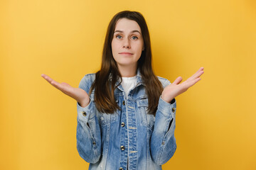 Clueless hesitant brunette woman spreads palms sideways stands doubtful cannot make decision, wears...
