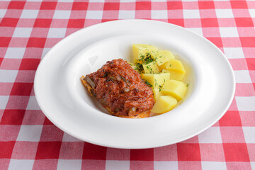 Grilled beefsteak, baked potatoes and fresh greenery. served in a white square plate over red plaid table cloth.