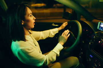Fototapeta na wymiar Young woman honking while driving car at night in the city.